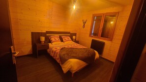 Une pièce chaleureuse avec un lit en bois, deux tables de chevet avec des lampes, une fenêtre et une décoration murale représentant une tête de cerf.