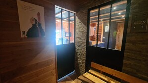 A wooden interior with a bench, a poster, and a door leading to a room with a stone wall and wooden ceiling. - CHALET 12-14 Persons 200 Metres from the slopes (Fontcouverte-la-Toussuire)