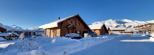 A wooden chalet with a sloped roof, surrounded by snow-covered mountains and a clear blue sky. - CHALET 12-14 Persons 200 Metres from the slopes (Fontcouverte-la-Toussuire)