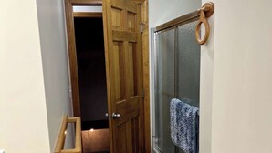 A narrow hallway with wooden flooring, a glass door with a towel hanging on it, and a wooden door with a handle. - The Hideaway: A Private Cabin in the North Maine Woods (Mount Chase)