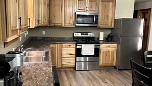 A kitchen with wooden cabinets, stainless steel appliances, granite countertops, and a wooden floor. - The Hideaway: A Private Cabin in the North Maine Woods (Mount Chase)