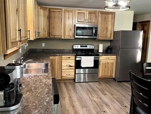 A kitchen with wooden cabinets, stainless steel appliances, granite countertops, and a wooden floor. - The Hideaway: A Private Cabin in the North Maine Woods (Mount Chase)