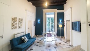 Un salon moderne avec un canapé bleu, une table à manger avec des chaises, un téléviseur fixé au mur et une grande fenêtre donnant sur un paysage verdoyant.