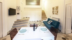 Un coin repas avec une table dressée pour deux personnes, un canapé et un escalier menant à l’étage supérieur.