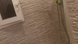 A shower area with a textured wall, a handheld showerhead, and a bottle of shampoo. - Private new flat (Bari)