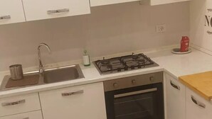 A compact kitchen with white cabinets, a stainless steel sink, a gas stove, and a built-in oven. - Private new flat (Bari)