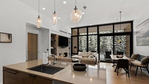 A modern kitchen with a central island, a dining area with a wooden table and chairs, and a cozy seating area with sofas. - Luxury Moonlight Basin 2 Bedroom Condo (Big Sky)
