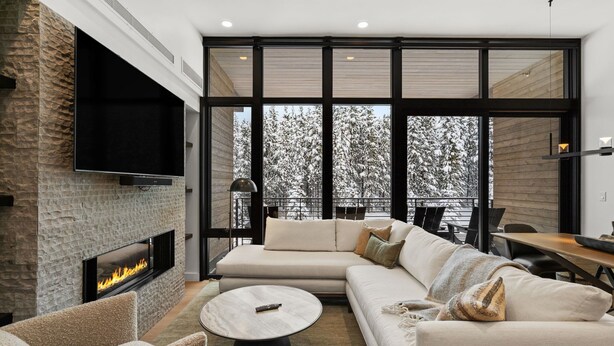 A modern living room with a fireplace, large windows, and a cozy seating area. - Luxury Moonlight Basin 2 Bedroom Condo (Big Sky)