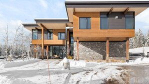 A modern two-story building with a stone facade and wooden accents, featuring large windows and a covered outdoor area. - Luxury Moonlight Basin 2 Bedroom Condo (Big Sky)
