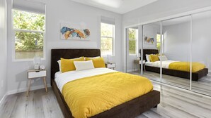 Ein modernes Schlafzimmer mit einem großen Bett, einem Nachttisch, einem Spiegel und Blick auf Grünfläche.