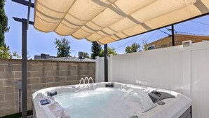 Ein Whirlpool mit Bedienfeld, umgeben von einem weißen Zaun, unter einer beigefarbenen Markise.