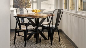 Un comedor con una mesa y sillas de madera, un tapete estampado y un ventanal con vistas a árboles.