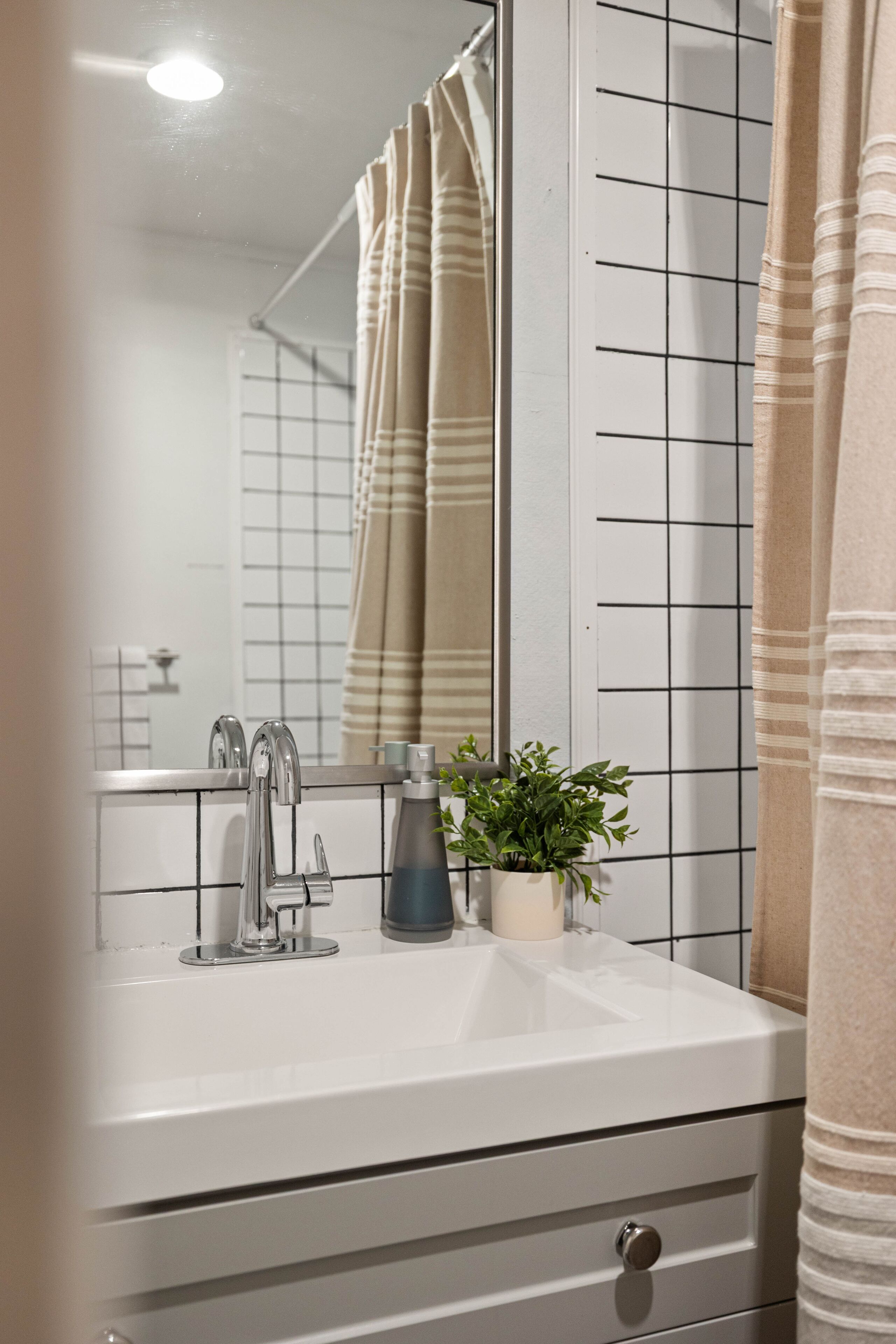 A bathroom with a white sink, a mirror, a potted plant, and a striped shower curtain.