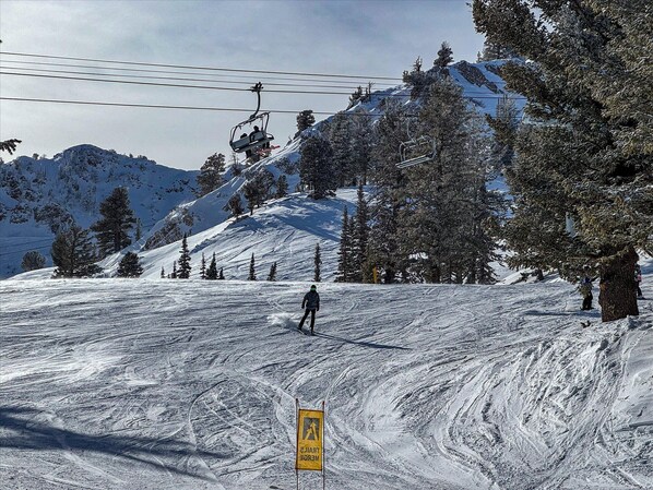 A ski slope with a chairlift, trees, and a sign indicating a pedestrian crossing.