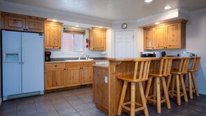 Una cocina con gabinetes de madera, un refrigerador blanco, un fregadero y una barra con taburetes.