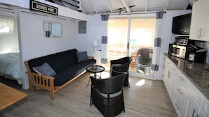 A compact living space with a sofa, two chairs, a small table, a kitchenette, and a sliding glass door leading to an outdoor area.