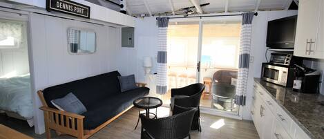 A compact living space with a sofa, two chairs, a small table, a kitchenette, and a sliding glass door leading to an outdoor area.
