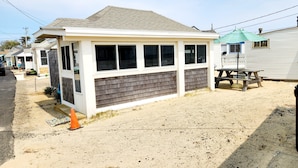 A small, single-story building with a sloped roof, a front porch, and a picnic table.