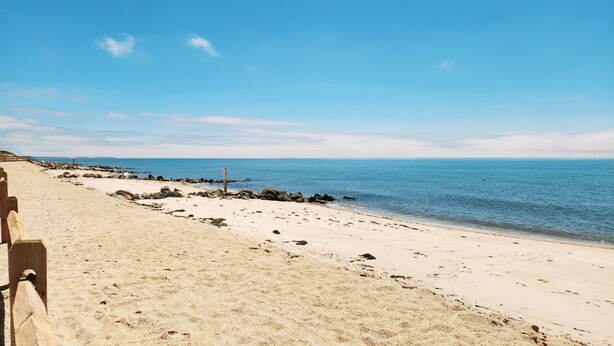 A beach with a wooden fence and a rocky shoreline.