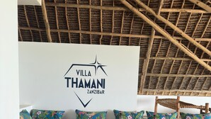 Een kamer met rieten dak, een zithoek met kleurrijke kussens, een houten salontafel en een kamerbreed tapijt met een patroon.