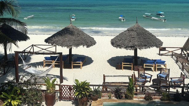 Een strand met rieten parasols, houten ligstoelen en uitzicht op de oceaan.