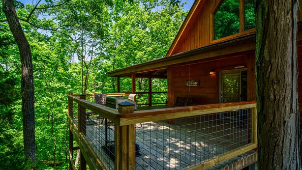 A wooden cabin with a balcony, surrounded by dense forest.
