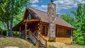 A log cabin with a stone chimney, wooden exterior, and a covered porch with a staircase.