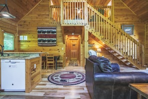 Interior acogedor de una cabaña con una escalera de madera, una zona de comedor y una sala de estar con un sofá de cuero.