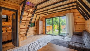 A cozy wooden cabin with a loft bedroom, a dining area, and a large sliding glass door to the backyard. - Karaöz Sapphire Bungalows (Kumluca)
