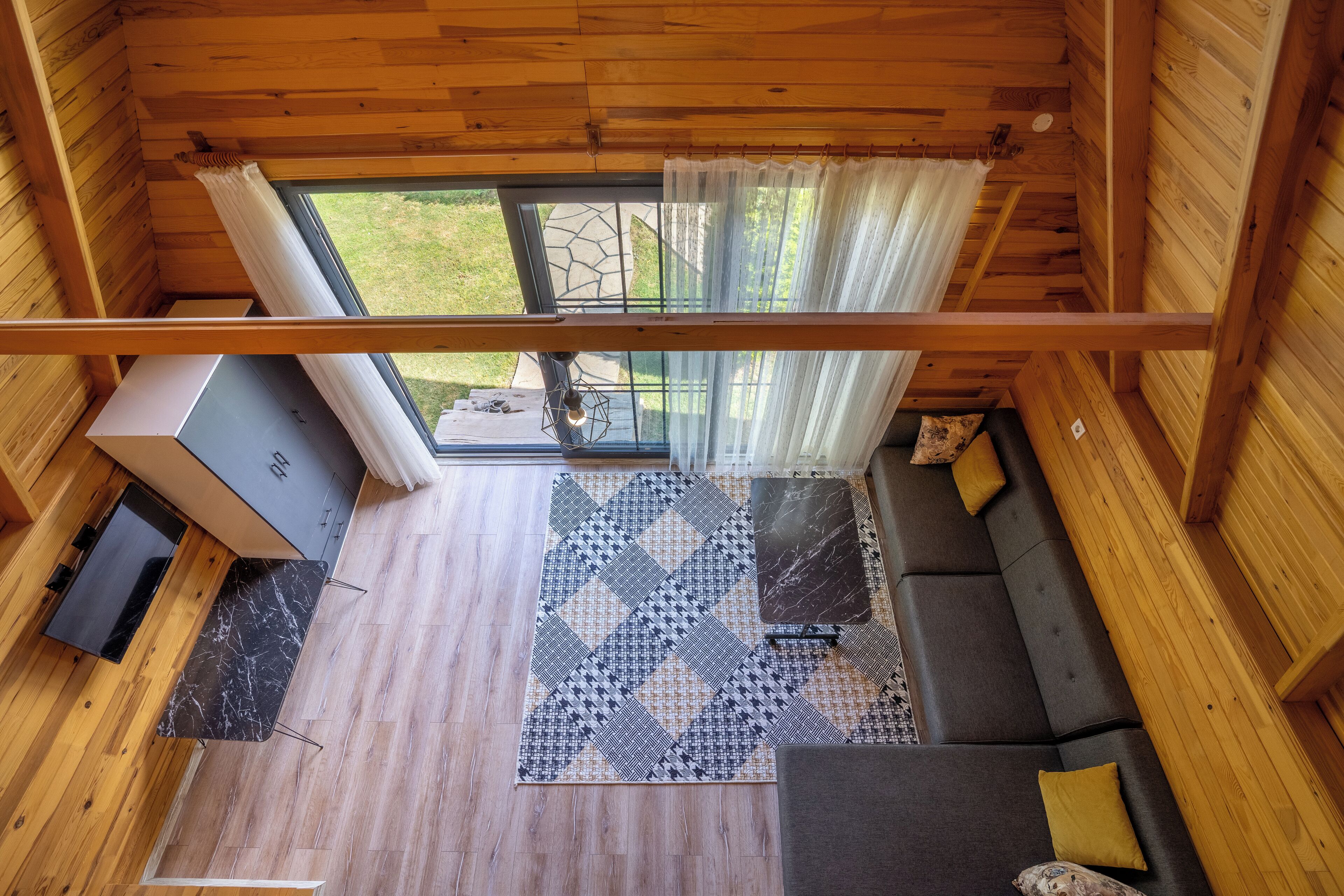 A wooden cabin interior with a sofa, a dining table, and a TV.