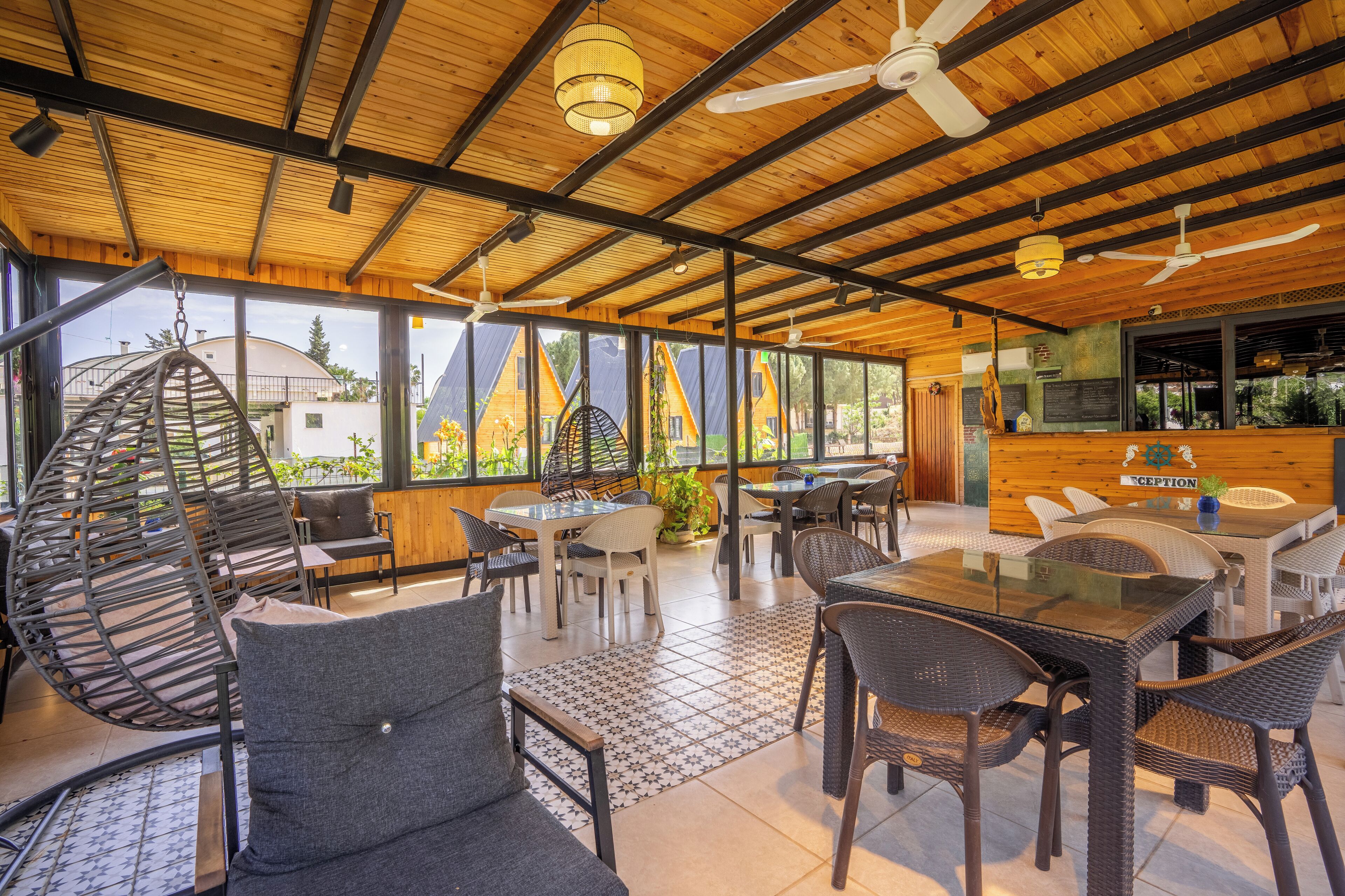 A spacious indoor area with wooden beams, large windows, and a variety of seating arrangements including tables and chairs.