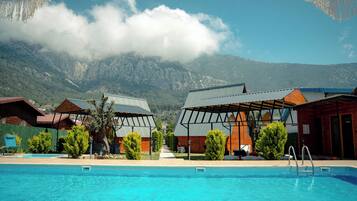 Piscina con montañas al fondo, edificios de madera y cielo despejado.