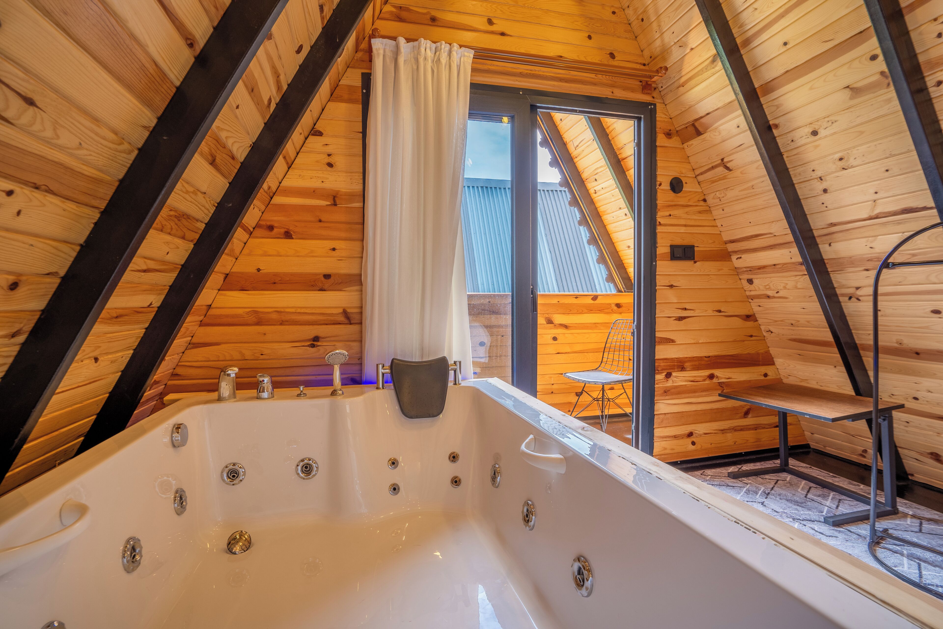 Una cabaña de madera con techo inclinado, una bañera grande y un amplio ventanal corredera que da a un área exterior.