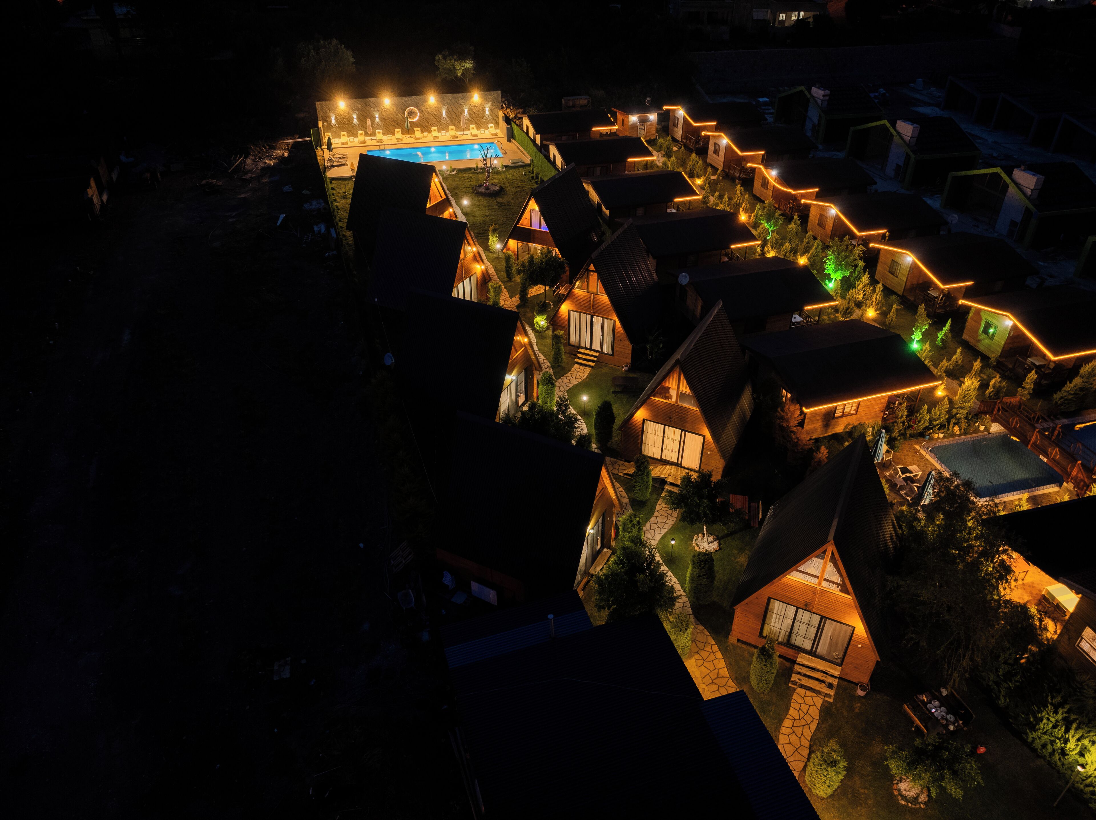 An aerial view of a resort with multiple cabins, a central pool area, and well-lit pathways.