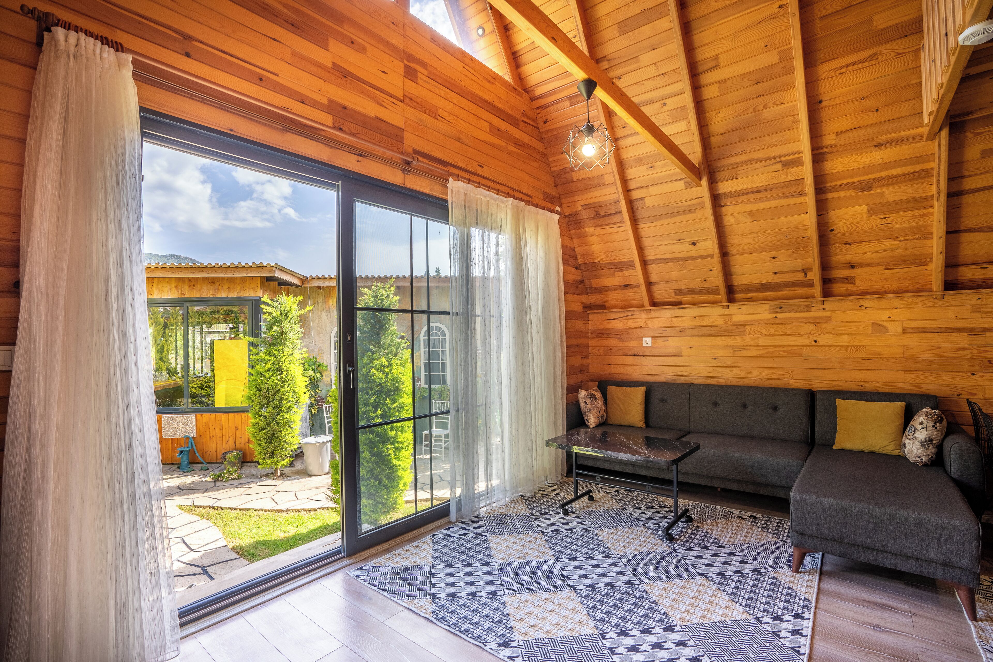 Amplia habitación con paredes de madera y un amplio ventanal corredera que da a un espacio exterior.