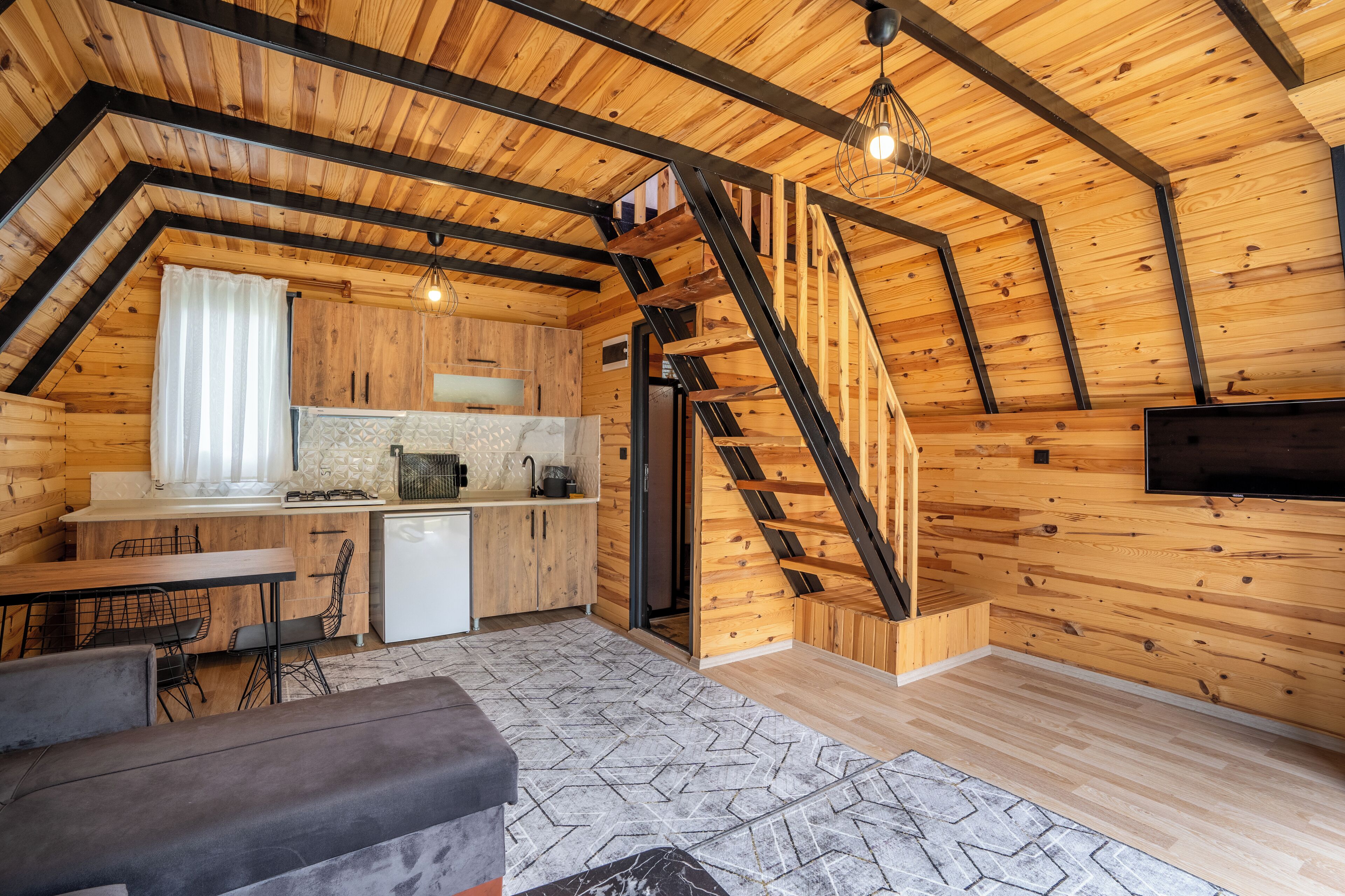 A cozy attic bedroom with a wooden sloped ceiling, a built-in desk, and a staircase leading to the upper floor.