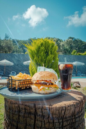 A meal with a burger, fries, and a soda on a wooden table outdoors. - Karaöz Sapphire Bungalows (Kumluca)