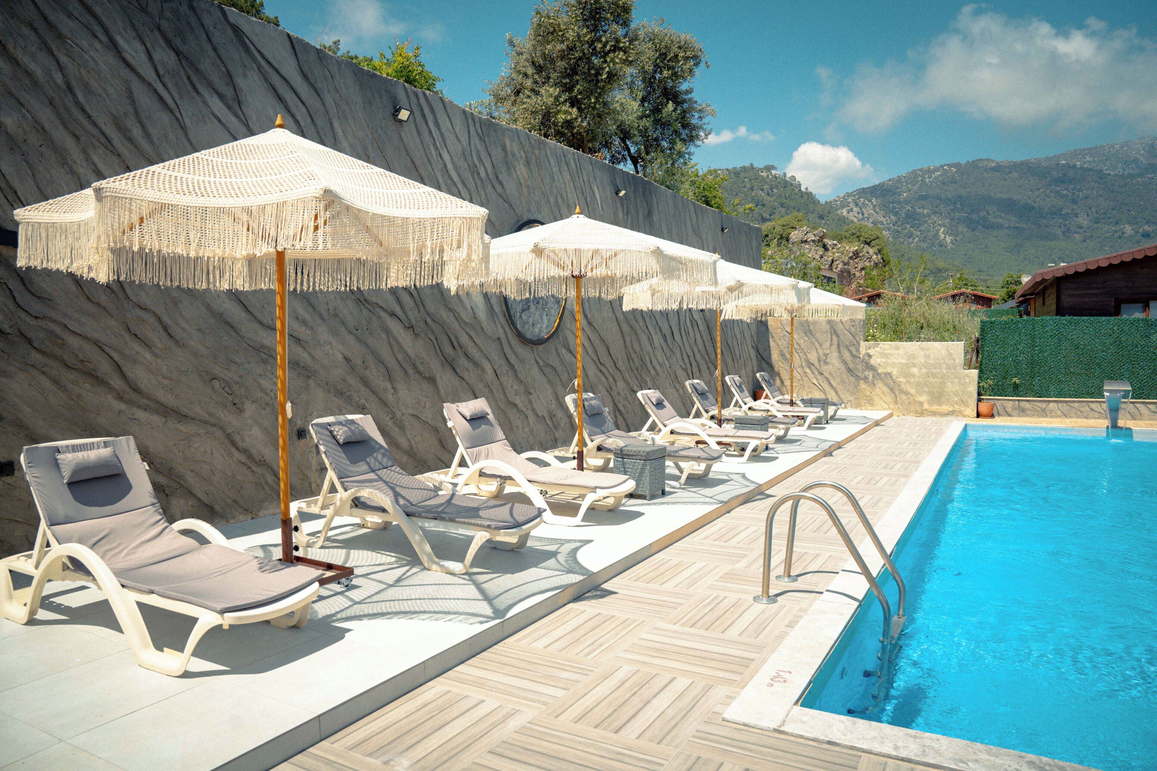 Zona de piscina con sillones de descanso y sombrillas, una piscina y un paisaje montañoso de fondo.