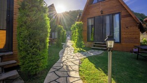 A wooden cabin with a stone pathway leading to the entrance, surrounded by greenery and a picnic table. - Karaöz Sapphire Bungalows (Kumluca)