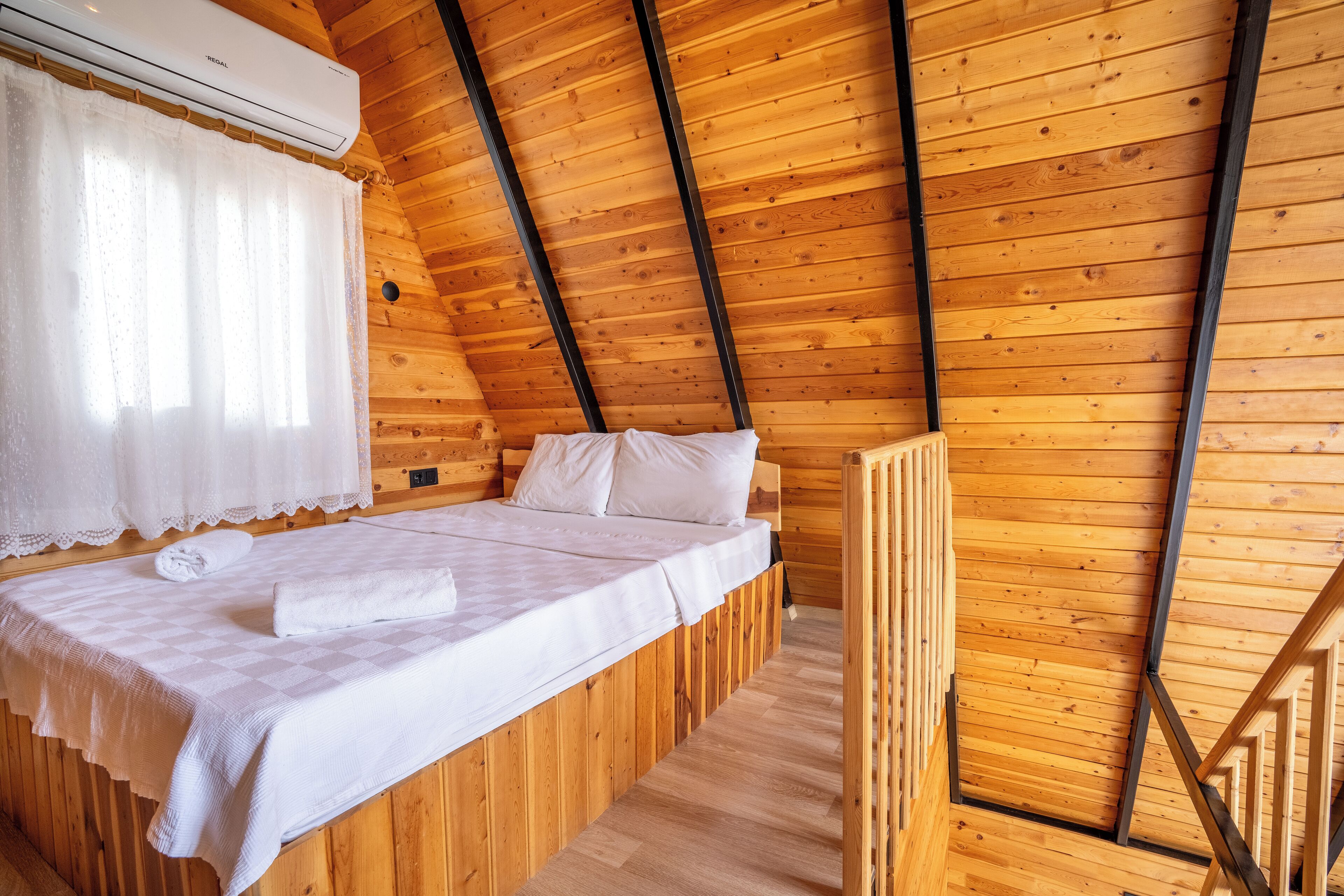 Quarto de cabana de madeira com cama, janela com cortinas e aparelho de ar condicionado.