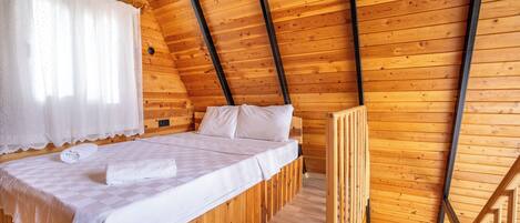 A wooden cabin room with a bed, a window with curtains, and an air conditioning unit.