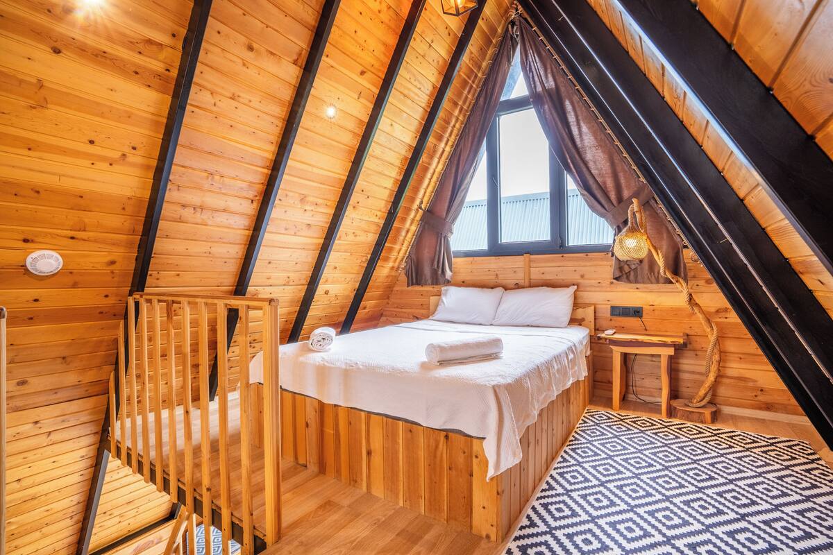 Uma cabana de madeira aconchegante com um quarto no mezanino, uma pequena mesa de madeira e um tapete estampado.