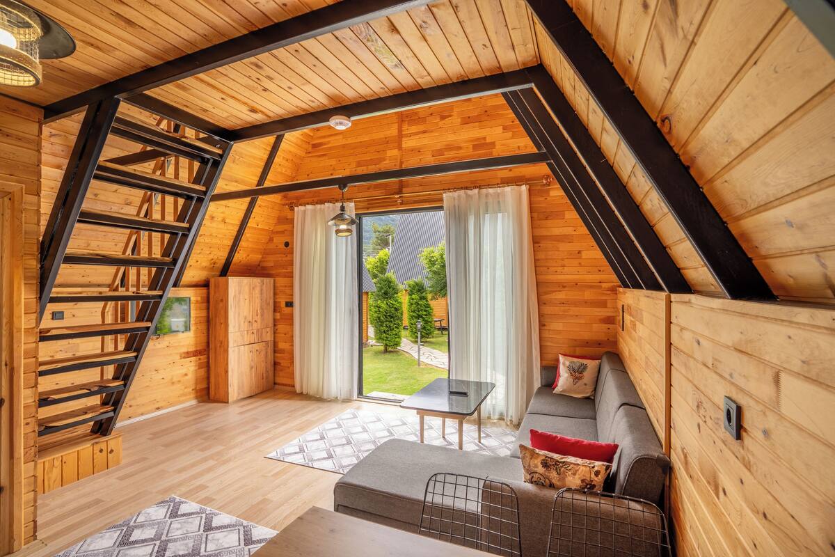 Quarto de sótão aconchegante com escada de madeira, um sofá e vista para um jardim através de uma porta de vidro.