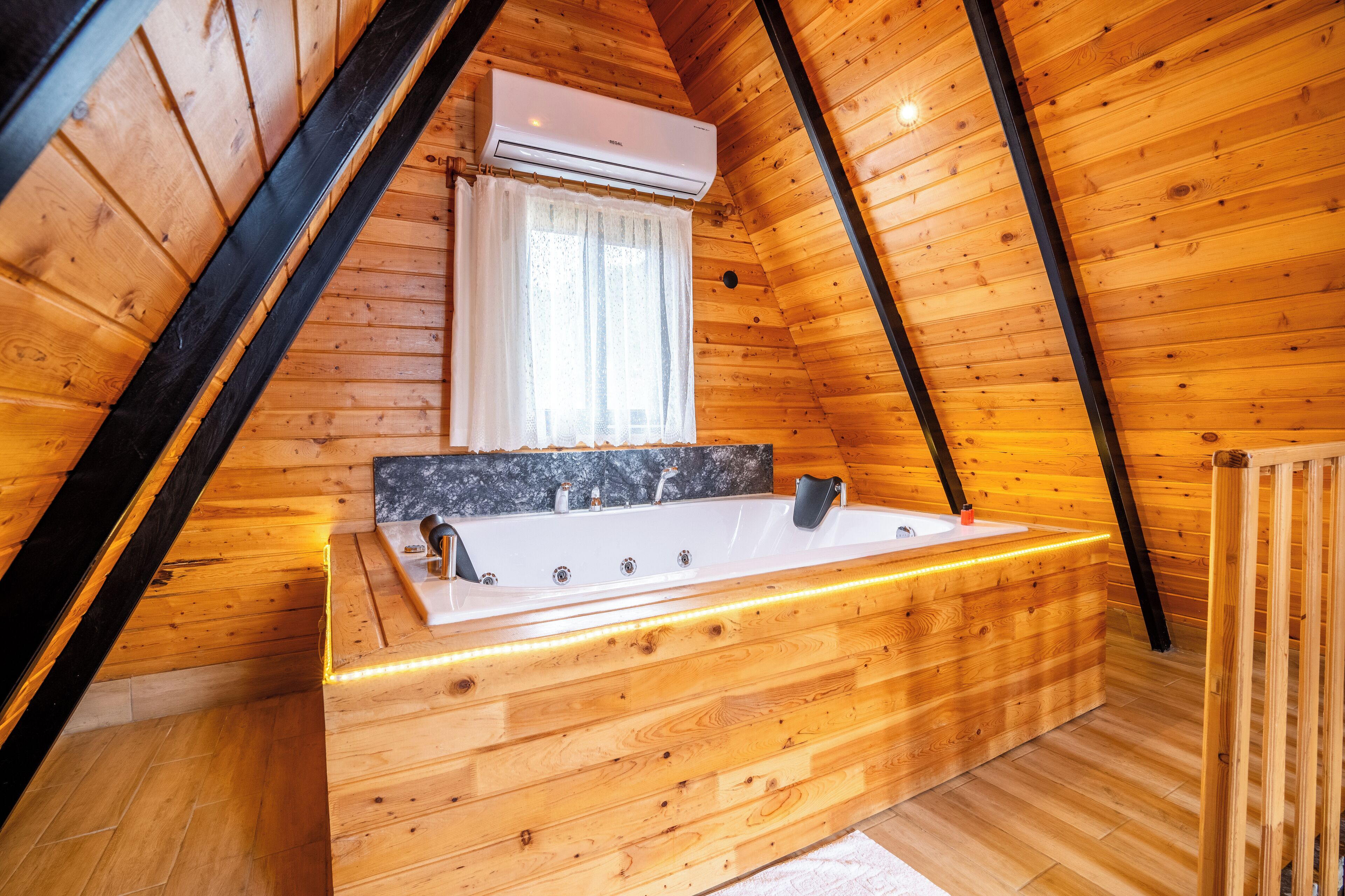 A wooden cabin with a wooden bathtub, a window with curtains, and an air conditioning unit.
