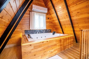 A wooden cabin with a wooden bathtub, a window with curtains, and an air conditioning unit. - Karaöz Sapphire Bungalows (Kumluca)