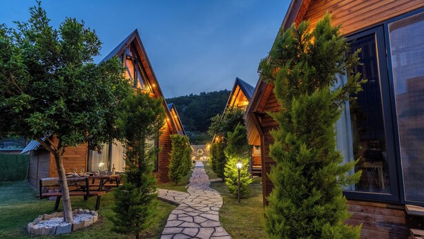 A row of wooden cabins with a stone pathway leading to a picnic table and a small building. - Karaöz Sapphire Bungalows (Kumluca)