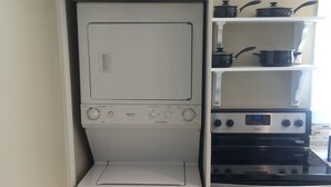 Una cucina compatta con lavatrice e asciugatrice integrate, un piano cottura e ripiani sopra per riporre oggetti.