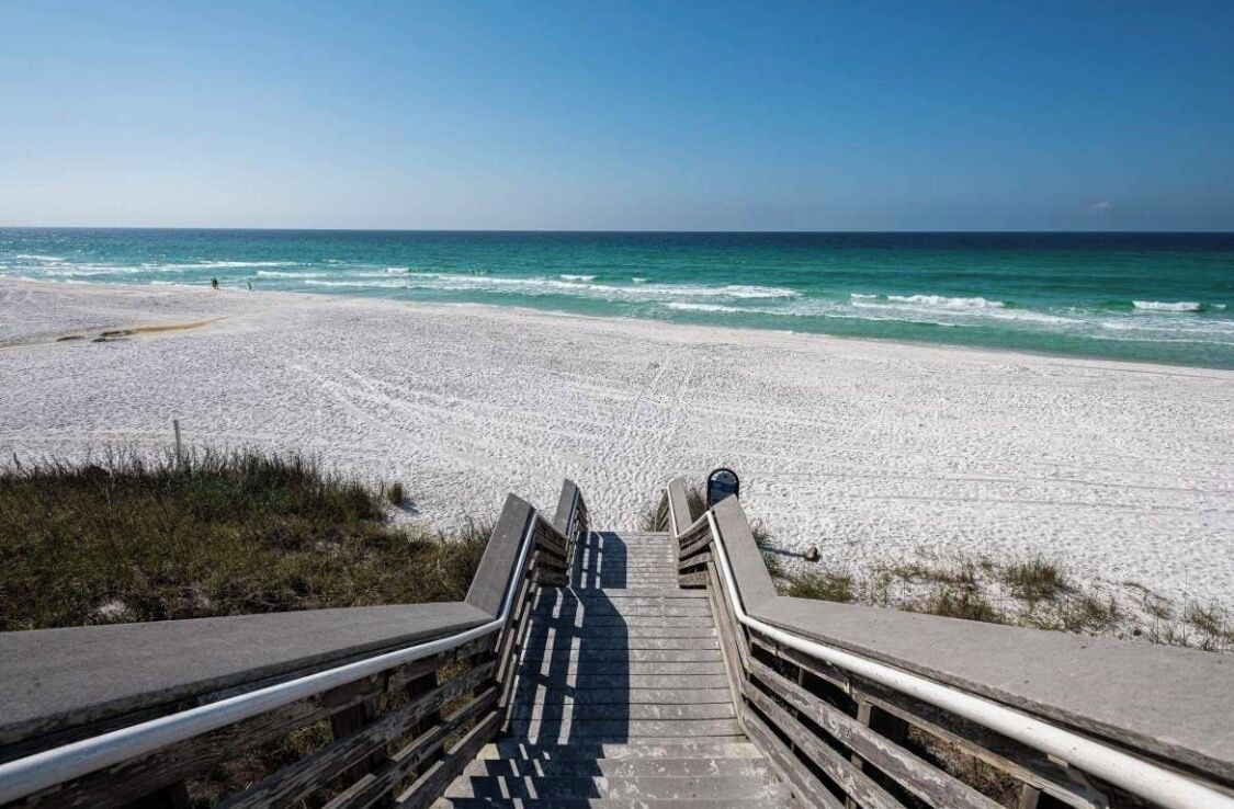 A beach with a wooden staircase leading down to the shore, surrounded by sand and ocean.