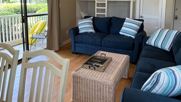 Un soggiorno con un divano blu, una poltrona bianca, un pouf in vimini e una ventola a soffitto.