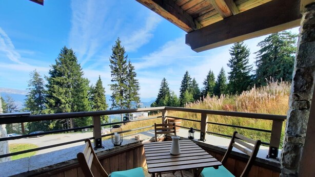 An outdoor deck with wooden furniture and a view of a forest and mountains.